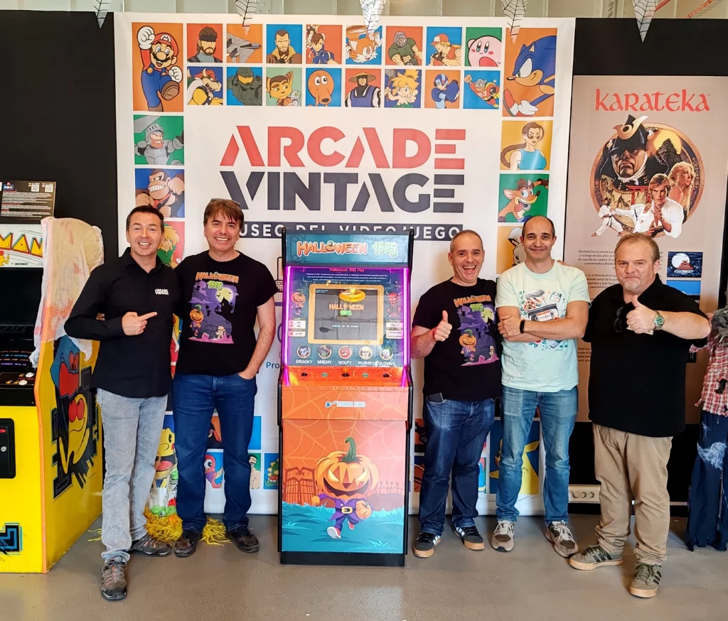 Javier y Guillermo de Spoonbox Studio junto a Eduardo y José María del Museo Arcade Vintage en Ibi, posando frente a la máquina arcade dedicada de Halloween 1985.